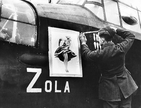 A Lancaster bomber crewman screws on a nose art painting of Zola on to the side of