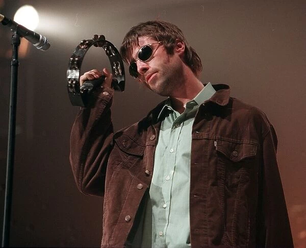 Liam Gallagher performing on stage playing a tambourine at an Oasis concert at the SECC