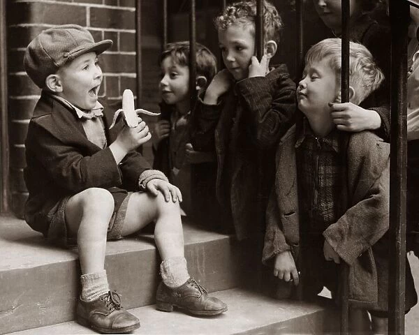 A Little boy holding a banana whilst other children gaze longingly at it hoping to try a