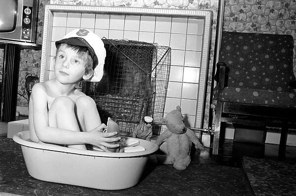A little boy wearing a sailors cap as he has a bath by the fire
