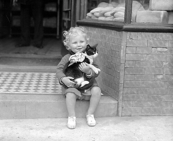 Little Girl With Cat A small child sitting on the steps of a shop holding a cat in