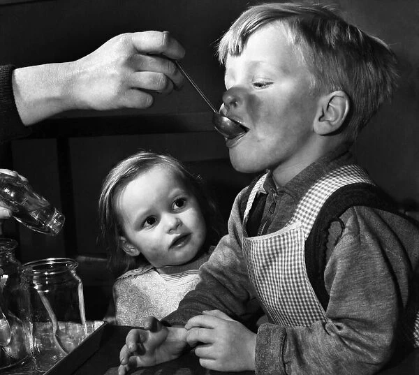 Little girl watches a boy being fed. February 1953 D740