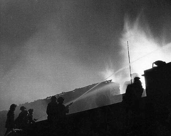 London firefighters tackling a timber fire from a wall in Camberwell. 8th December 1940
