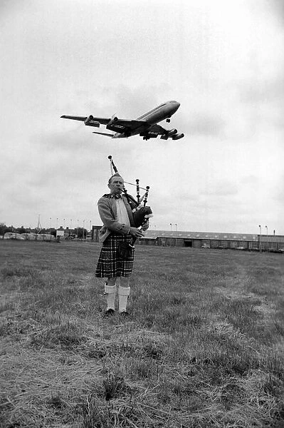Lone bagpipe player Jim Thomas playing as a jumbo jet flies overhead May 1975
