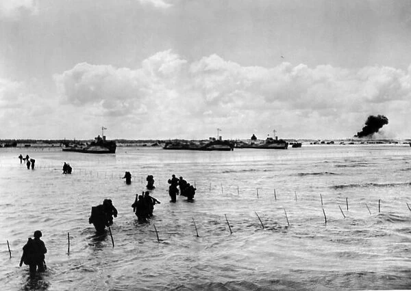 A long line of U.s army men wade through shallow water off northern coast of France to