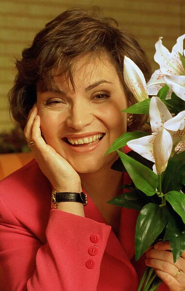 Lorraine KELLY next to a green white plant red jacket watch