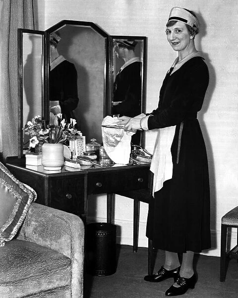 A maid standing by a dresser mirror polishing the silver, March 1938