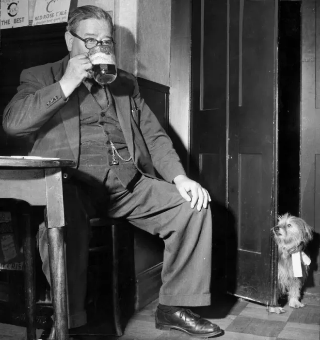 Framed Print : A man drinking a pint at his local pub, has been followed by his pet dog who looks on Framed Print : A man drinking a pint at his local pub, has been followed by his pet dog who looks on