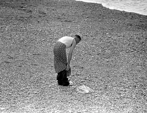 A man getting undressed on the pebble beach at Brighton as he prepares to for a swim