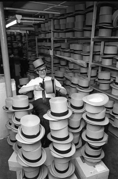 Framed Print : Man happily brushing top hats at a suit hire company in preparation for Royal Ascot