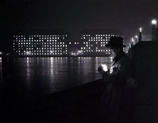 A man lights a cigarette on the Thames embankment in London Circa 1955 people