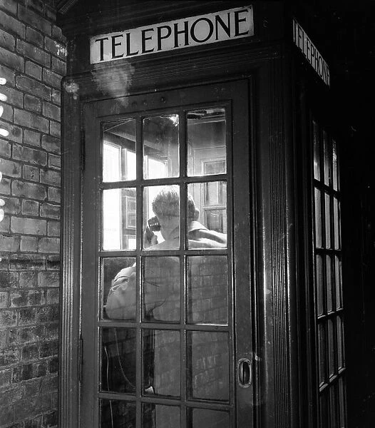 A man making a phone call from a public telephone box. 25th October 1957