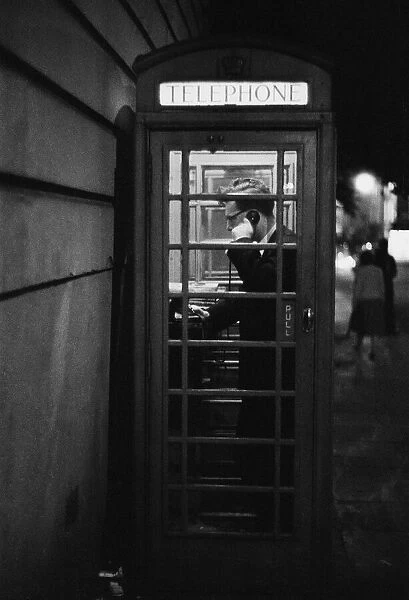 A man making a call from a public telephone box in London. 31st August 1958