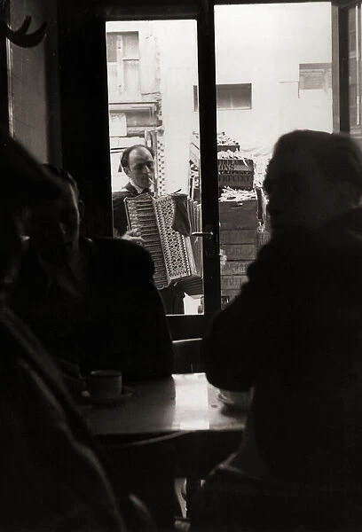 man playing accordian to people sitting in cafe smoking