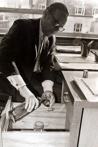 A man pours himself a drink which he keeps hidden in a filing cabinet in his office at