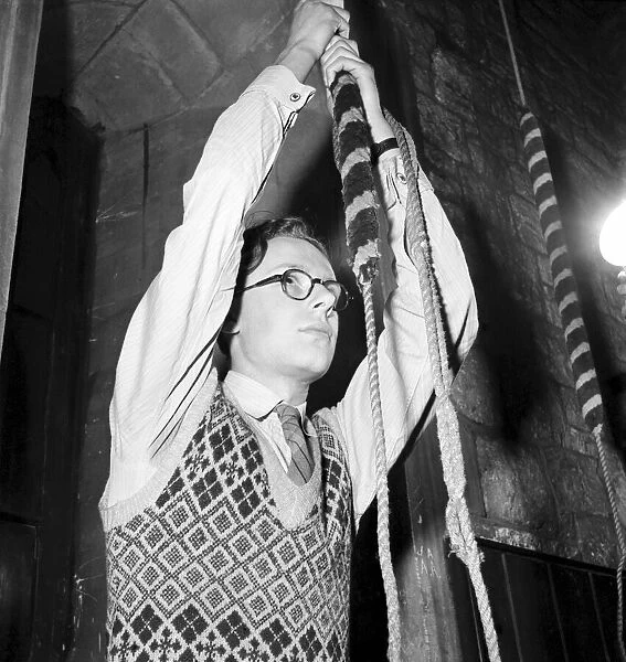 A man pulling a long cord to ring a bell in his church. December 1953 D7601