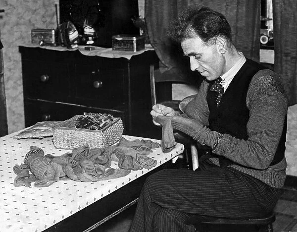 A man sits at his table darning his socks, February 1937