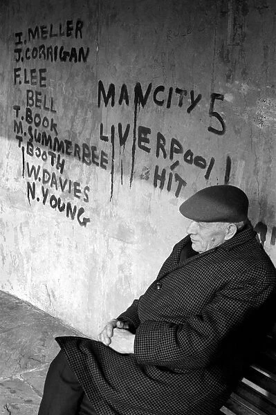 Man sitting on a bench at a bus shelter covered with graffiti after a football match