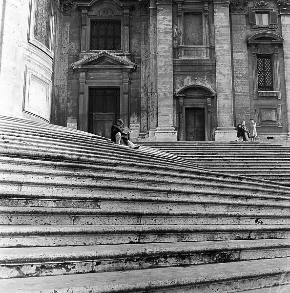 A man sitting on the steps of St Maria Maggiore, reading a newspaper. Rome, Italy
