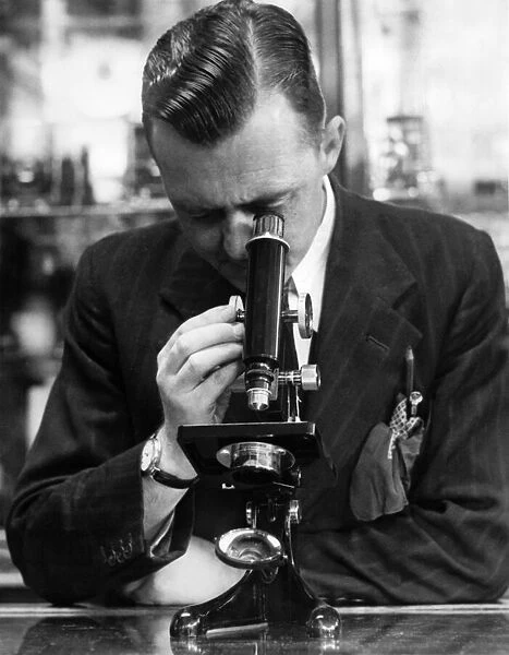 A man studying a specimen under a microscope. July 1947 P009567
