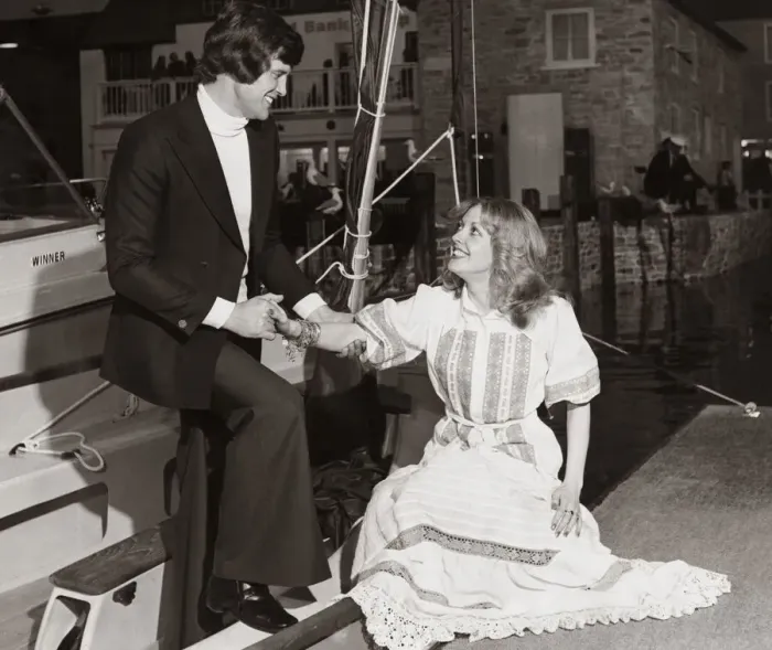 Framed Print : Man wearing a navy blue blazer white polo sweater and trousers helps a lady out of a boat