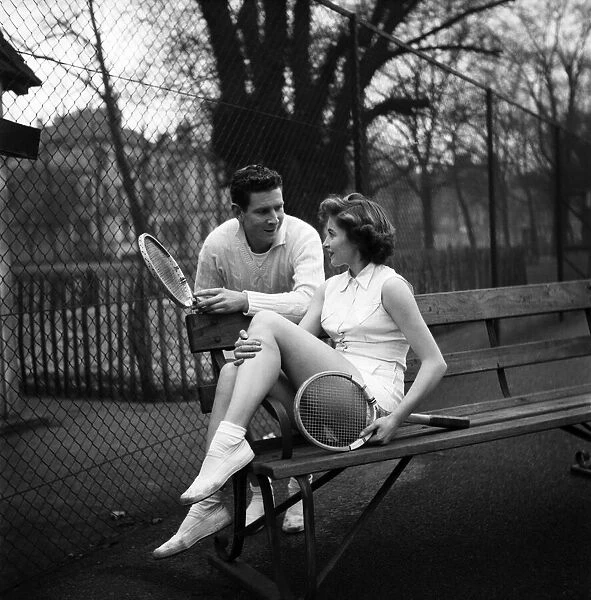Man and woman talking on a park bench after enjoying a game of tennis January 1953