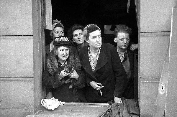 A man and four women with a kitten look out a window at the bomb damage in Kentish Town