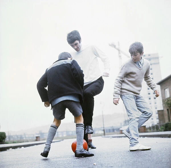 Manchester United footballer George Best playing football in the street with two young