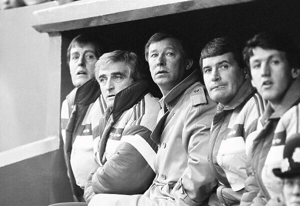 Manchester United manager Alex Ferguson sits in the dugout with coaching staff during