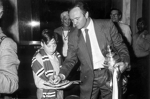 Manchester United manager Ron Atkinson signs an autograph for a young fan whilst holding