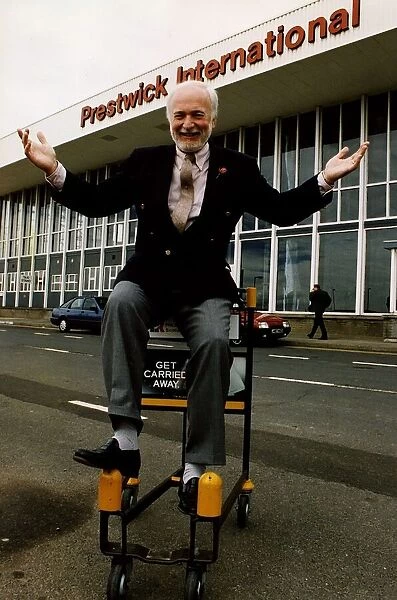 Matthew Hudson sitting on luggage trolly with hands in the air outside Prestwick Airport