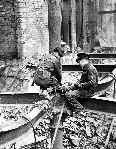 Members of H. M Forces perched on a girder as they place a charge of gelignite in position