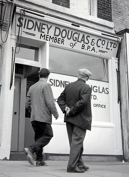 Two men walking past Sidney Douglas betting shop in Mile End Road London May 1961