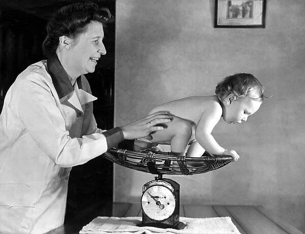 A midwife weighs a toddler in her scales during a check up July 1943 A©
