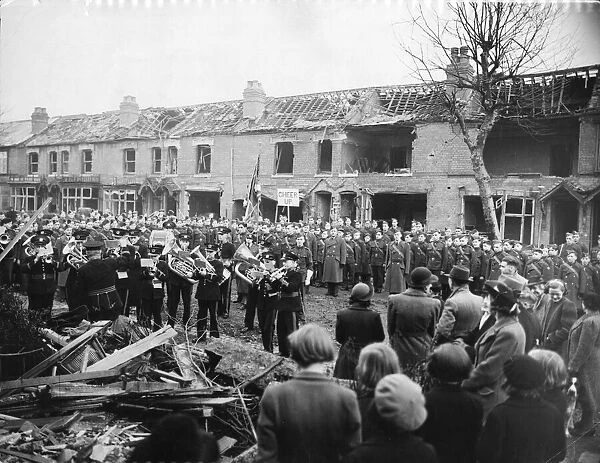 A military band perform some music infant of a row of houses that have been destroyed in