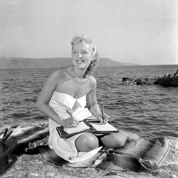 Miss Billie Love, holiday maker in Plymouth, sits down on the beach to write letters to