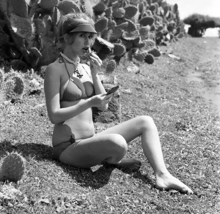 Framed Print : Model putting on her make up as she poses on a beach in Africa wearing a bikini