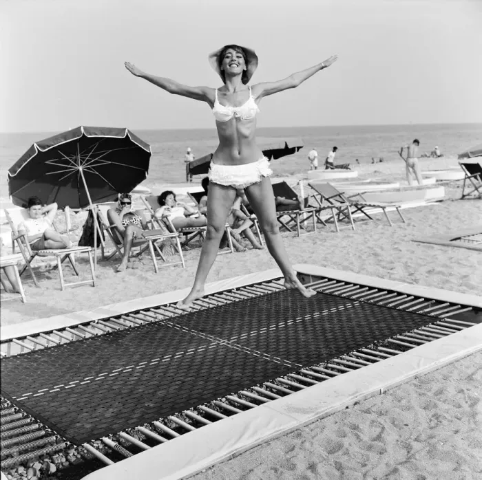 Framed Print : A model wearing bikini swimwear bounces on a trampoline on a beach in the French Riviera