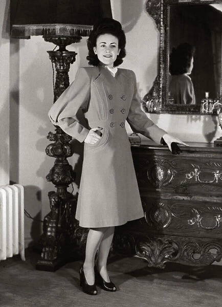 A model wearing a harella coat with new shaped sleeves and flared skirt standing beside a