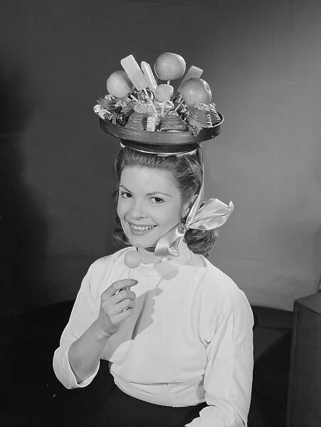 Model wearing a hat made from chocolate and fruit. Circa 1960