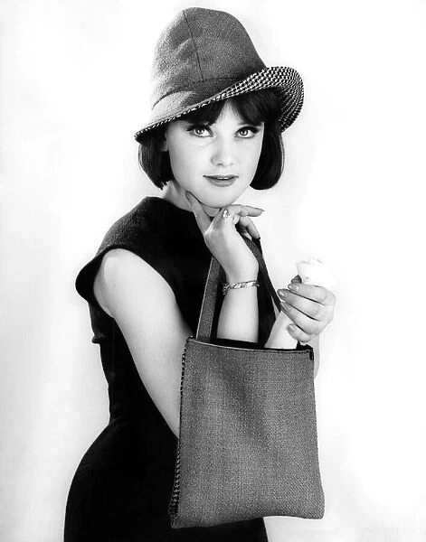 Model wearing a sleveless black dress and hat whilst holding a shopping handbag