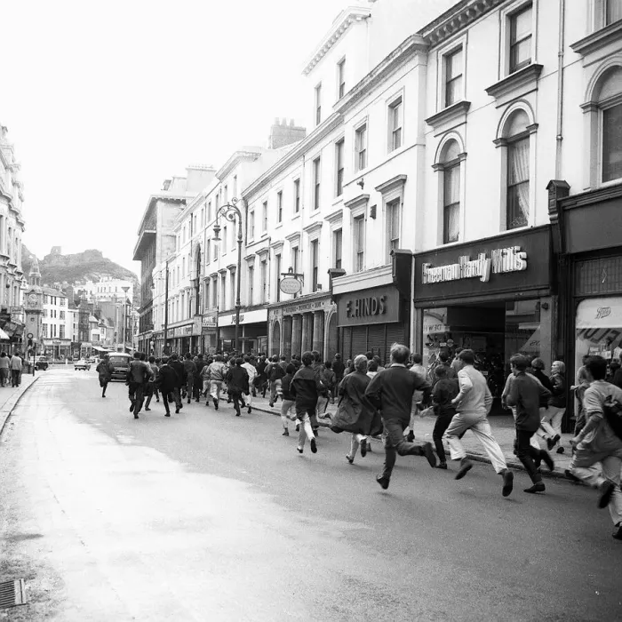 Framed Print : Mods run down the road outside shops in Hastings