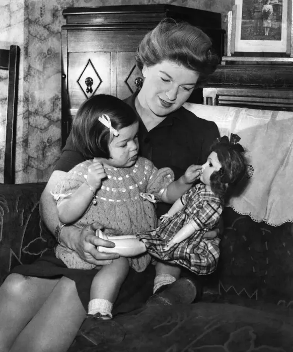 Framed Print : Mother and child at home, the girl playing with her doll as she sits on mummys lap Framed Print : Mother and child at home, the girl playing with her doll as she sits on mummys lap