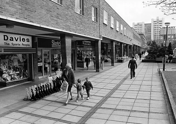 A mother and two young boys walk past the shops in Smithford Way, Coventry
