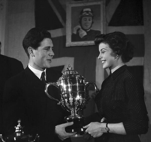 Motorcycle racing champion Geoff Duke shows the trophy to film star Joan Rice