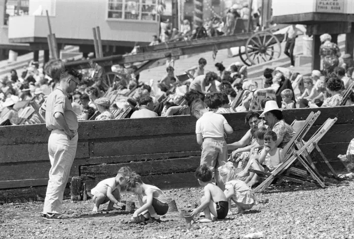 Framed Print : Mum enjoys a sandwich and dad looks on as children build sand castles on the beach