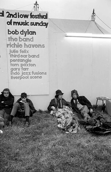 Music fans at The Isle of Wight Festival with a poster of Artists performing behind