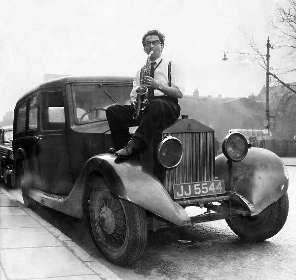 Musician Johnny Roadhouse sitting on the bonnet of a car playing his saxophone