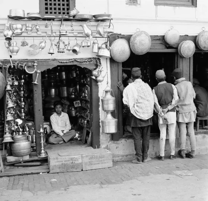Framed Print : A Nepalese shopkeeper sits in his ironmongers store while shoppers browse his neighbours