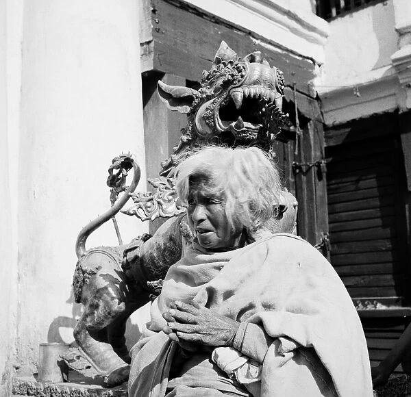 Nepalese woman poses beside a sculpture of a Dragon dog guarding a shrine in Katmandu